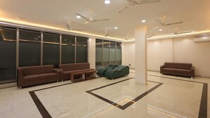 A modern waiting area with two sofas, a coffee table, and a green chair. - Hotel Anmol One  (Indore)