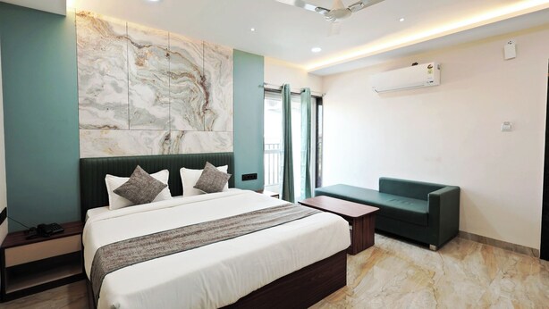 A modern hotel room with a large bed, a green sofa, a marble wall, and a ceiling fan. - Hotel Anmol One  (Indore)
