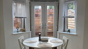 A dining area with a round table, four chairs, and two windows with blinds.