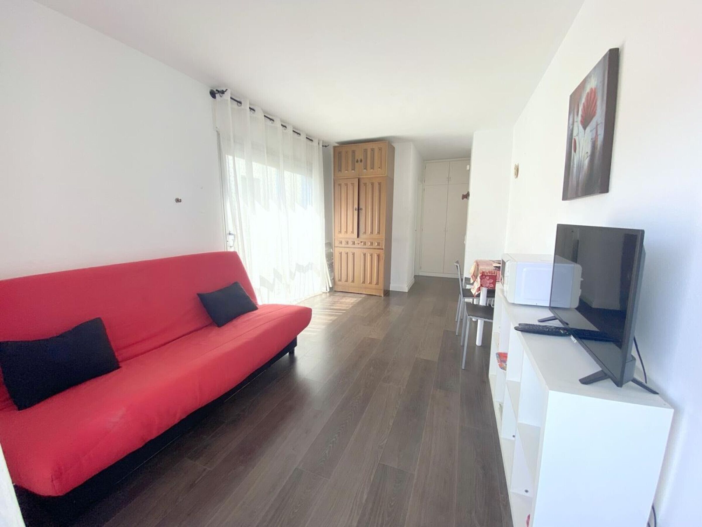 A living room with a red sofa, a TV, and wooden cabinets in the background.