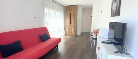 A living room with a red sofa, a TV, and wooden cabinets in the background.