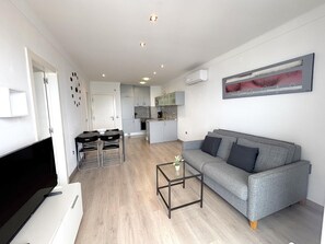A modern living room with a grey sofa, a coffee table, and a TV. - Renovated beachfront apartment with AC and balcony in Roses (Roses)