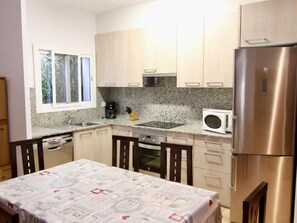 A compact kitchen with a stainless steel refrigerator, a microwave, a stove, and a sink. There is a window above the sink, and the kitchen has wooden cabinets and a granite countertop.