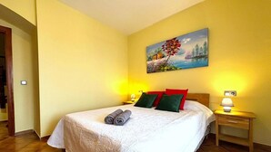 Hotellihuoneessa on sänky, kaksi yöpöytälamppua, taulu seinällä ja ovi vasemmalla puolella.