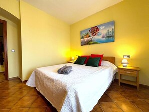 Ein Hotelzimmer mit einem Bett, zwei Nachttischlampen, einem Bild an der Wand und einer Tür links.