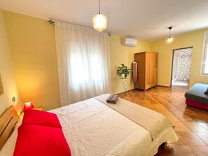 A room with a bed, a red chair, a mirror, a wardrobe, and a small table with a plant. - Charming Private House with Garden, 300m from Canyelles Beach - Sleeps 6, Roses, Spain (Roses)