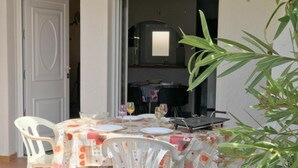 An outdoor dining area with a table set for two, surrounded by white plastic chairs, a potted plant, and a door. - Charming House in Roses: Private Terrace, Pool, A/C, Parking, Sleeps 4 (Roses)
