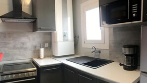 A compact kitchen with a stove, microwave, sink, and coffee maker. - Charming House in Roses: Private Terrace, Pool, A/C, Parking, Sleeps 4 (Roses)