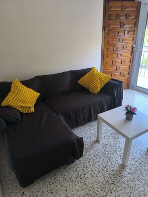 A dark brown sofa with two yellow pillows, a white table with a potted plant, and a speckled floor. - Casacasini 1A Charming 1-bedroom house with AC ,Balcony & Terrace in Málaga (Málaga)