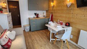 Una cocina compacta con armarios grises, una mesa de comedor blanca y una zona de estar acogedora con un sofá y cojines decorativos.