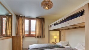 Una habitación pequeña con una cama litera, un aparador de madera, una ventana con cortinas y una lámpara colgante.