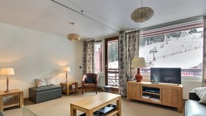Una sala de estar moderna con sofá, sillón, mesa de centro, mueble para televisión y vista a una pista de esquí.