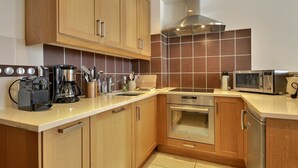 Una cocina moderna con gabinetes de madera, campana extractora de acero inoxidable, horno empotrado, microondas y cafetera.