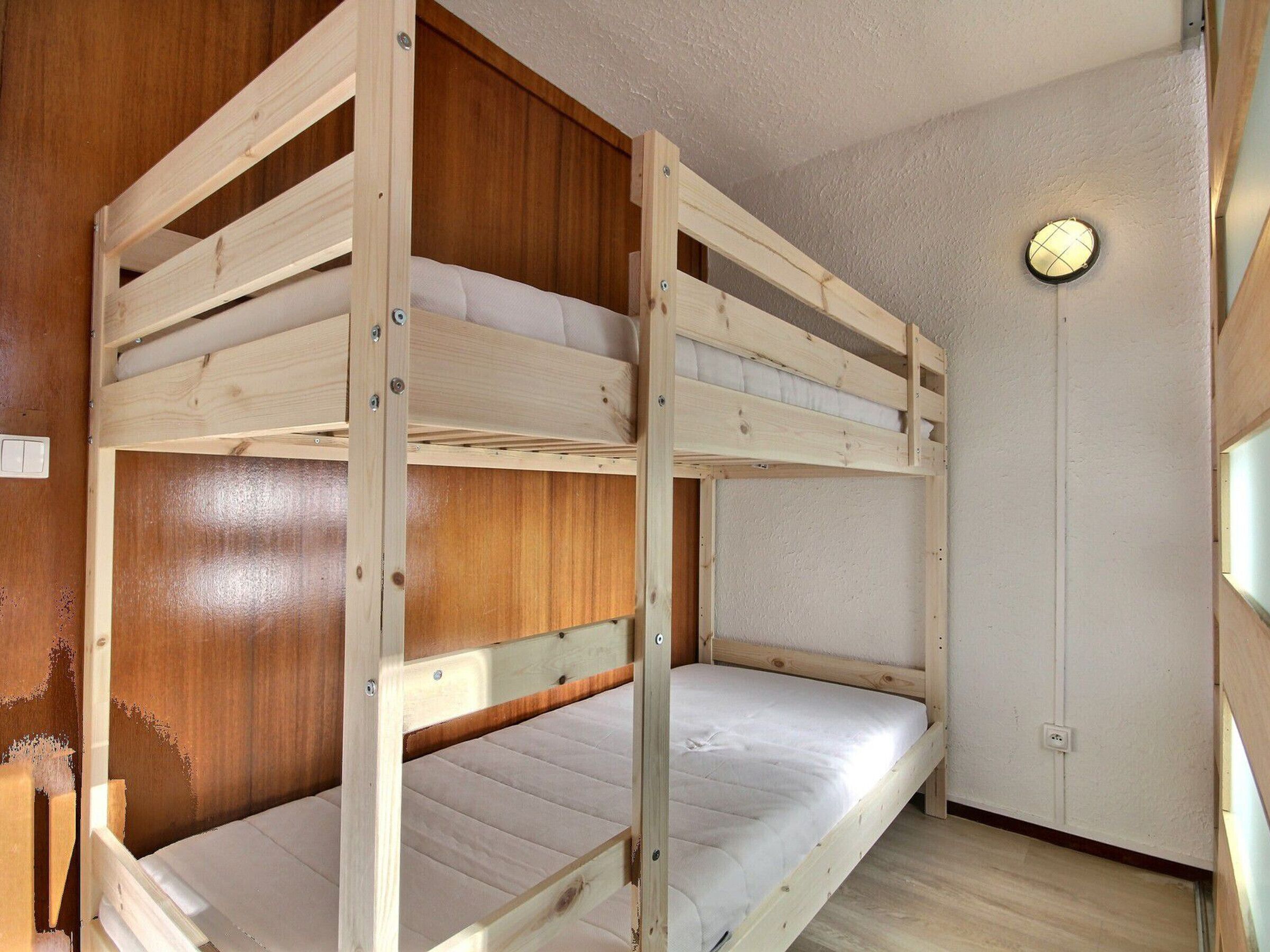 Une chambre avec des lits superposés, des murs en bois et une seule porte.