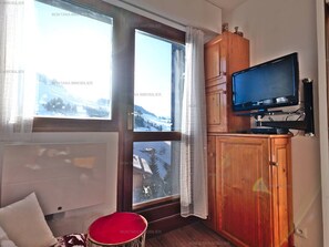 A room with a large window, a wooden cabinet, a television, and a red chair. - Studio + mountain corner for 4 pers. in Chinaillon (Le Grand-Bornand)