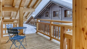 Eine Holzterrasse mit Tisch und Stühlen, mit Blick auf eine schneebedeckte Landschaft und eine Hütte.