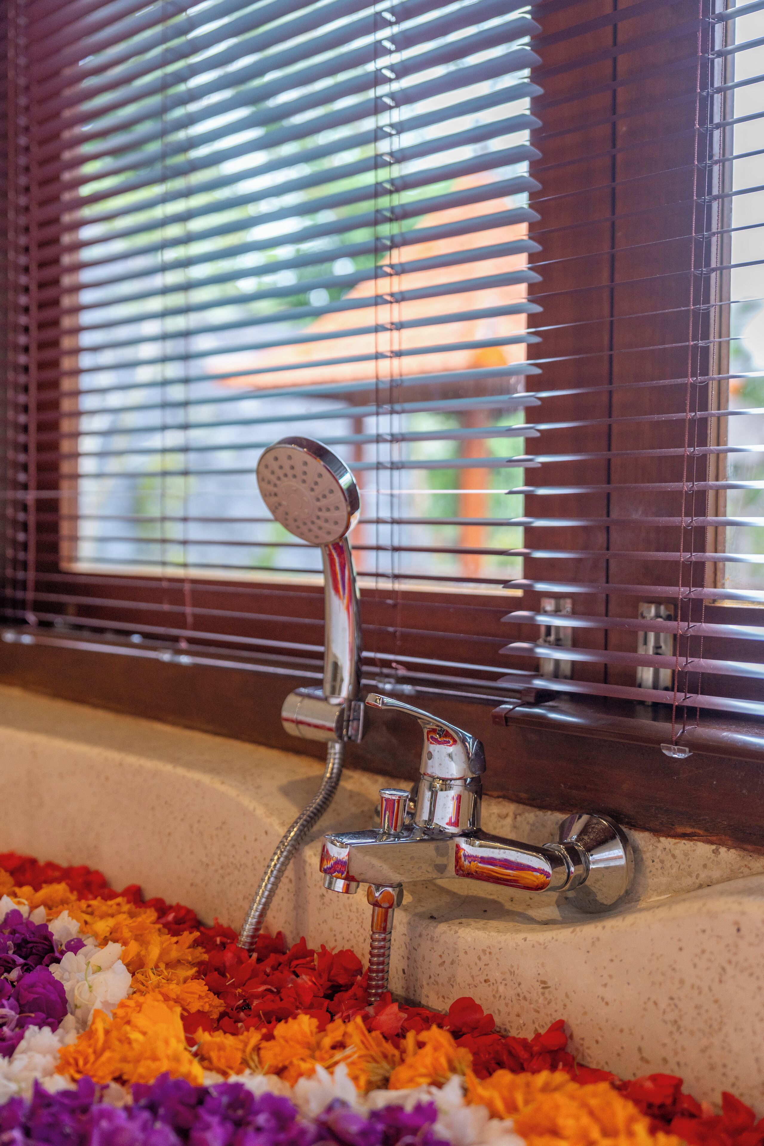 Un baño con ducha, una ventana con persianas y un lavabo decorado con pétalos de flores.