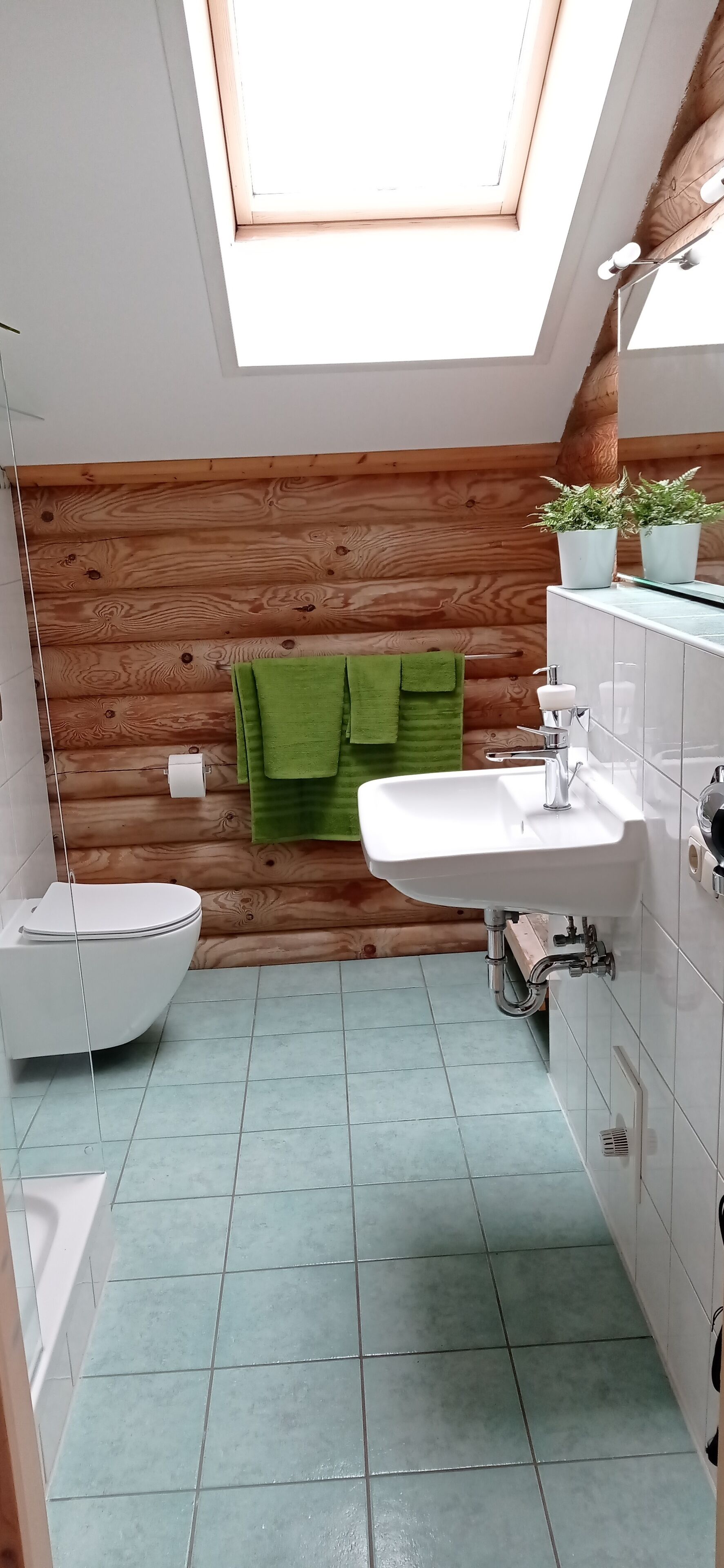 Un baño con tragaluz, un lavamanos blanco, una toalla verde y un inodoro blanco.