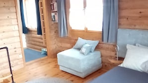 Ett sovrum i en stuga med träpanel, inrett med en säng, en soffa och ett fönster med gardiner.