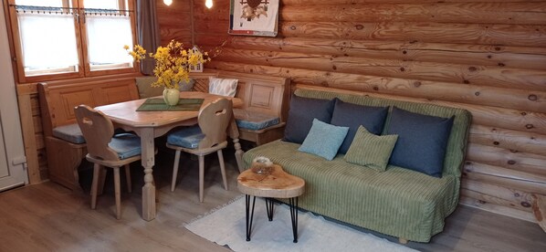 A cozy cabin interior with a wooden dining table, chairs, a sofa, and a small side table.