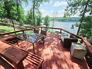 A wooden deck with glass-top tables and chairs, overlooking a lake with boats and a forested shoreline. - Log Home Hot Tub Retreat, Kayaks (Creal Springs)
