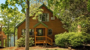 Une cabane en bois avec une véranda, une petite terrasse et une vue sur un lac.