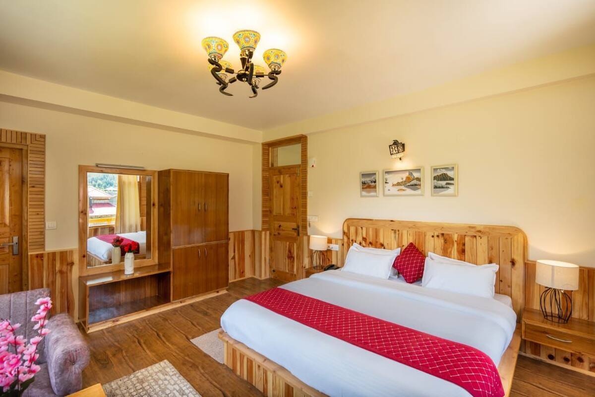 A bedroom with a large bed, wooden wardrobe, a mirror, and a chandelier.