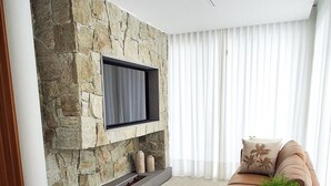 Una sala de estar moderna con una pared de acento de piedra, un televisor de pantalla plana, un sofá color beige, una pequeña mesa redonda y una planta en maceta.