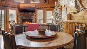 Een gezellig cabin interieur met een houten eettafel, stoelen, een open haard, een kerstboom en een opgezette hert.