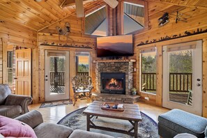 Ein gemütliches Blockhaus-Interieur mit Kamin aus Stein, Holzwänden und einem großen Fernseher.