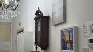 A hallway with a chandelier, a wall-mounted clock, framed artwork, and a thermostat. - zara'shome (Venezia)