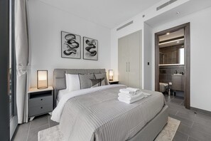 Ein modernes Schlafzimmer mit einem großen Bett, Nachttischlampen, einem Kleiderschrank und einem durch eine offene Tür einsehbaren Badezimmer.