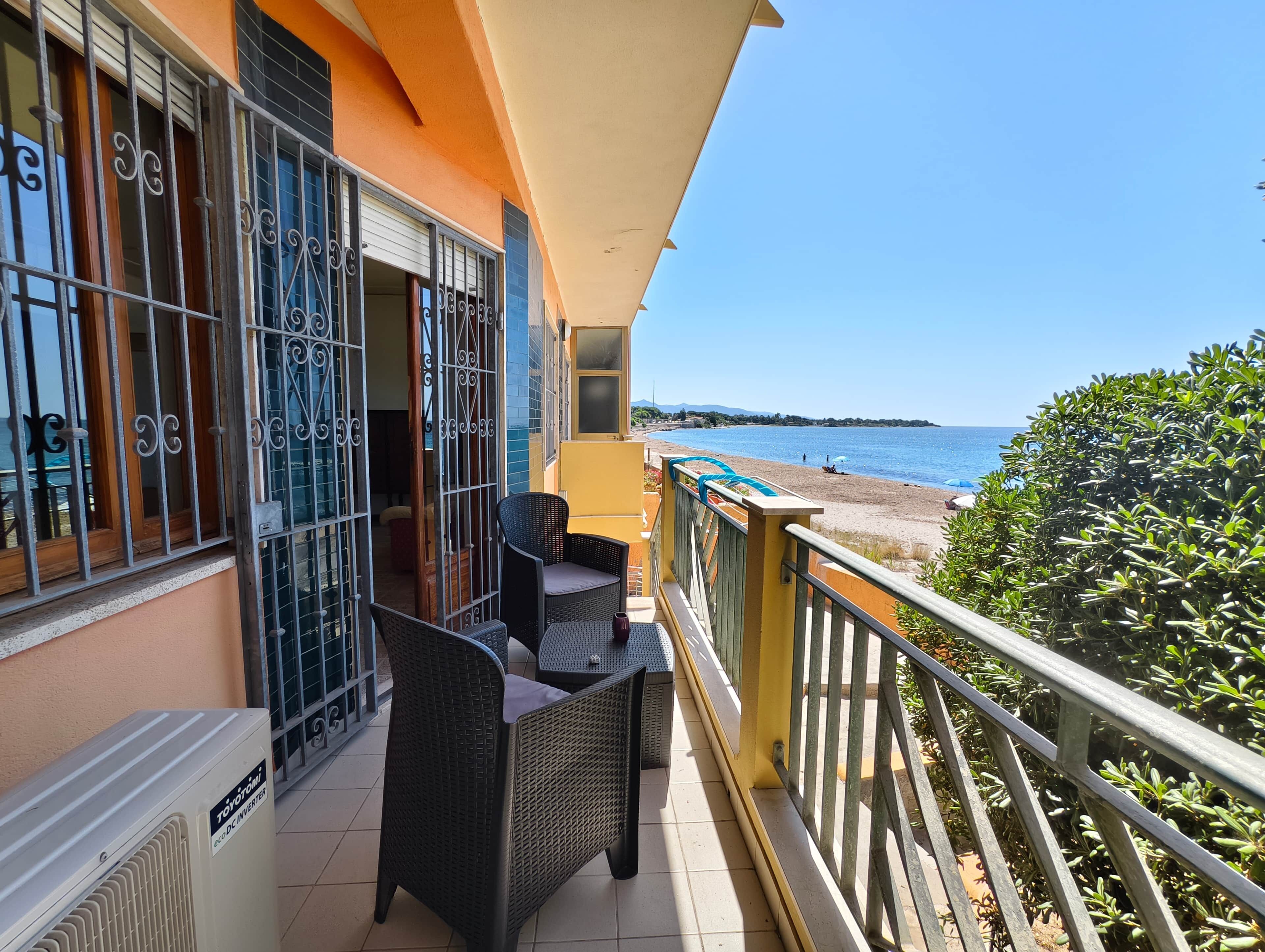 Un balcon agrémenté de meubles en osier, une vue sur la mer et un immeuble aux murs orange et aux balustrades en métal.