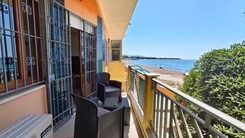 Un balcon agrémenté de meubles en osier, une vue sur la mer et un immeuble aux murs orange et aux balustrades en métal.