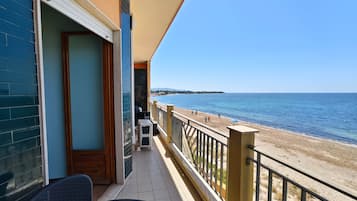 Un balcon avec vue sur la mer, une chaise et une petite table.
