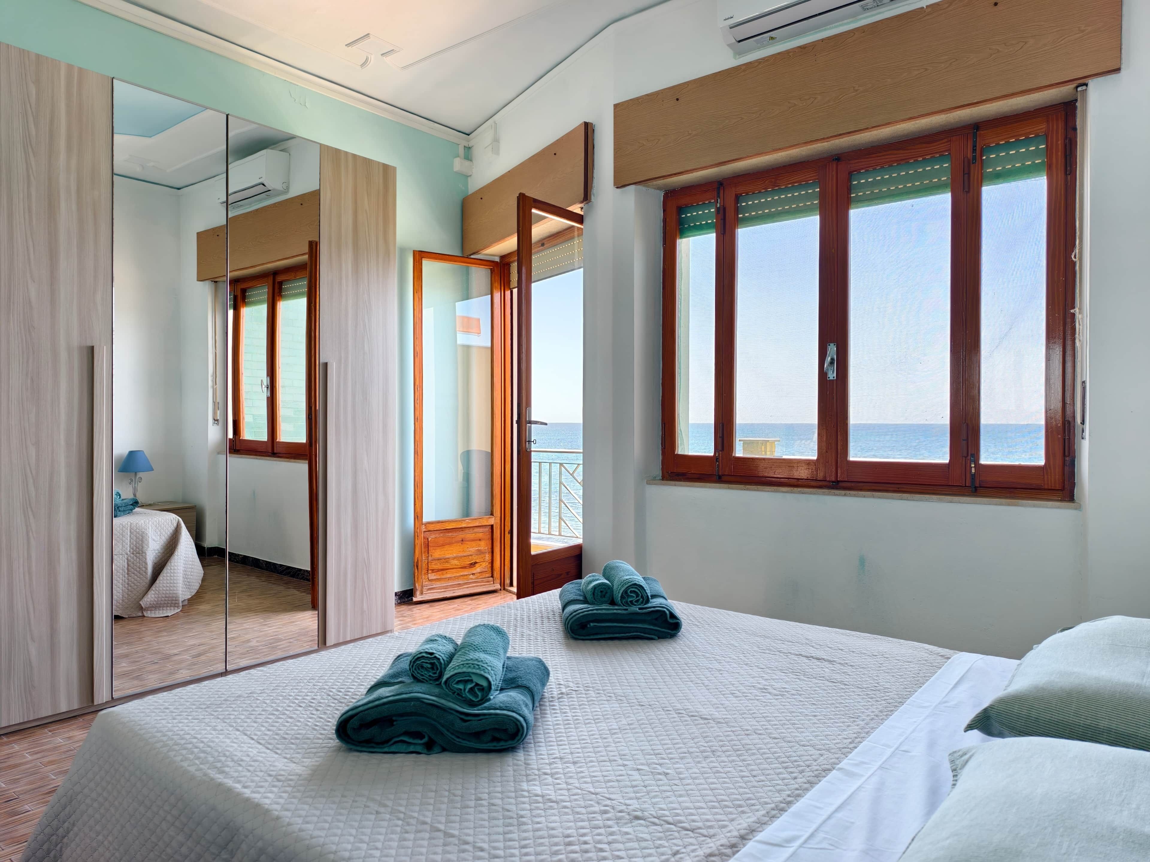 Une chambre d’hôtel avec un lit, un miroir, une fenêtre donnant sur un paysage agréable et une porte menant à un balcon.