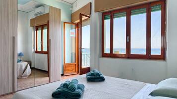 Une chambre d’hôtel avec un lit, un miroir, une fenêtre donnant sur un paysage agréable et une porte menant à un balcon.