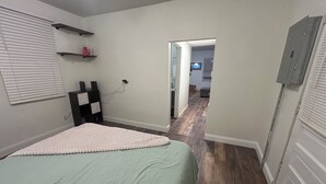 A bedroom with a bed, a desk, and a chair. There is a window with blinds, a shelf with items, and a door leading to another room. - Perfect 1-bedroom apartment with in welcoming Belleville (Belleville)