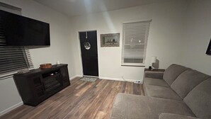 A living room with a flat-screen TV, a dark wooden entertainment unit, a grey sofa, and a door with a 'welcome' sign. - Perfect 1-bedroom apartment with in welcoming Belleville (Belleville)
