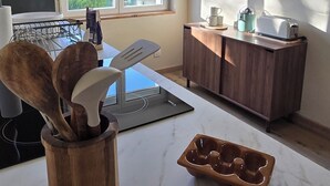 A kitchen with a marble countertop, wooden utensils holder, a toaster, and a window with a view of greenery.