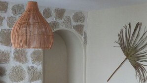 A cozy living room with a stone wall, a wooden dining table, a white chair, a bean bag, and a hanging plant.