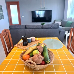 A living room with a sofa, a television, a dining table with chairs, and a fruit basket. - Villa La Yuca: private pool, barbecue area, and private parking (pet-friendly) (Los Alcázares)