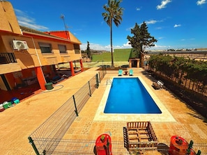 A swimming pool with a fenced area, lounge chairs, and a view of a residential area with a palm tree. - Villa La Yuca: private pool, barbecue area, and private parking (pet-friendly) (Los Alcázares)