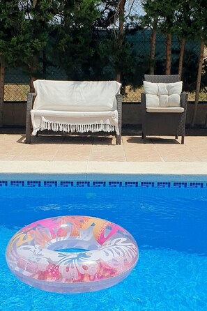 A swimming pool with a floating ring, a white covered sofa, and a wicker chair. - Villa La Yuca: private pool, barbecue area, and private parking (pet-friendly) (Los Alcázares)