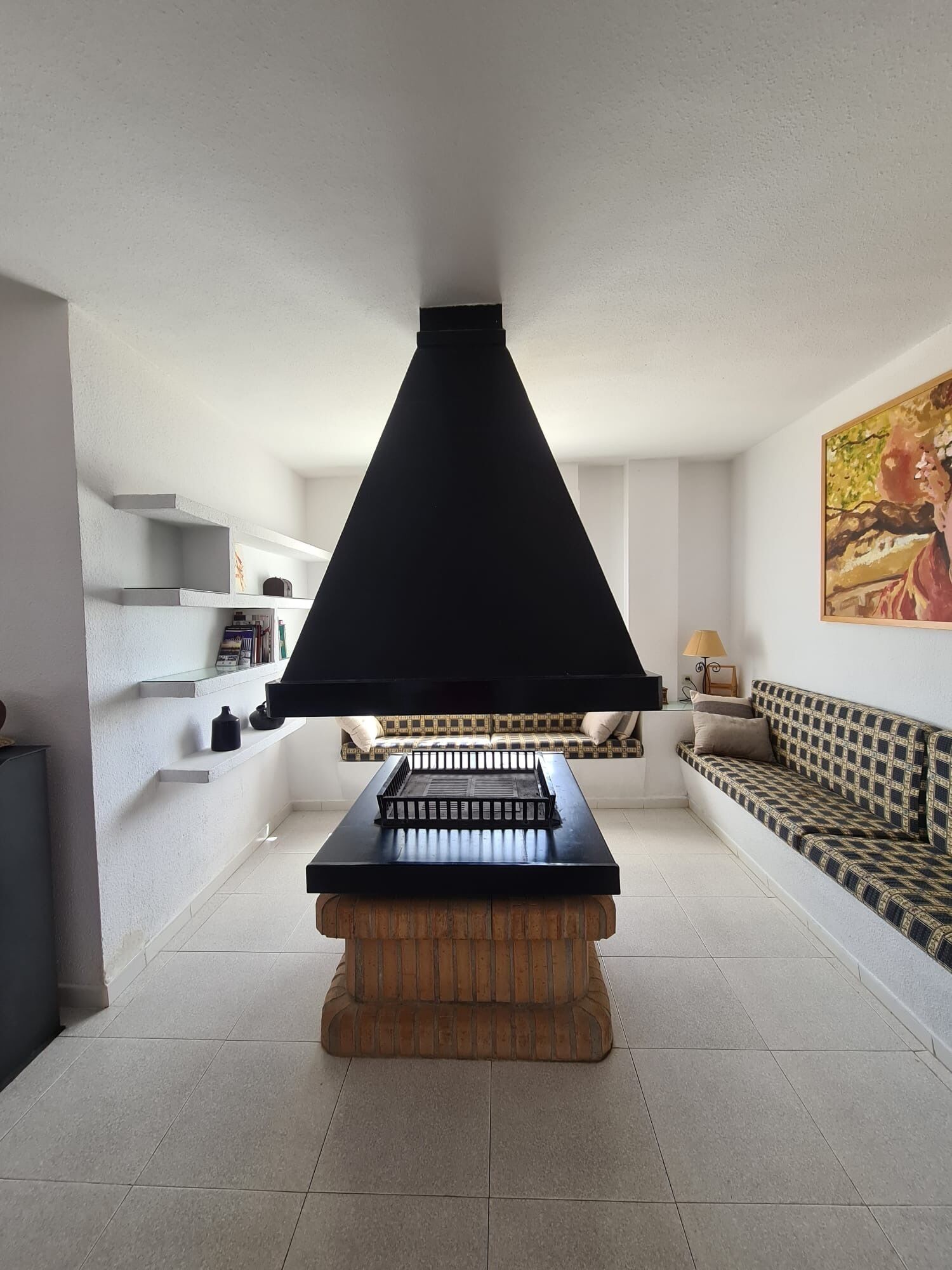 A modern living room with a black piano, a brick fireplace, a patterned sofa, and a painting on the wall.