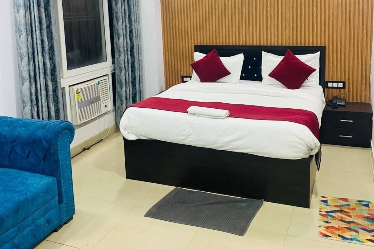 Un dormitorio ordenado con cama, un sillón azul, ventilador de techo y pared de paneles de madera.