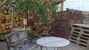 Eine Terrasse mit einer Metallbank, einem runden Tisch und einem kleinen Baum.