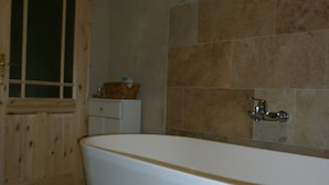 Ein Badezimmer mit freistehender Badewanne, einer Holztür und einer Fliesenwand.