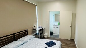 Un dormitorio con cama, escritorio y baño visible a través de una puerta abierta.