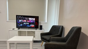 Una sala de estar moderna con un televisor de pantalla plana, una mesa de centro blanca y dos sillones oscuros.